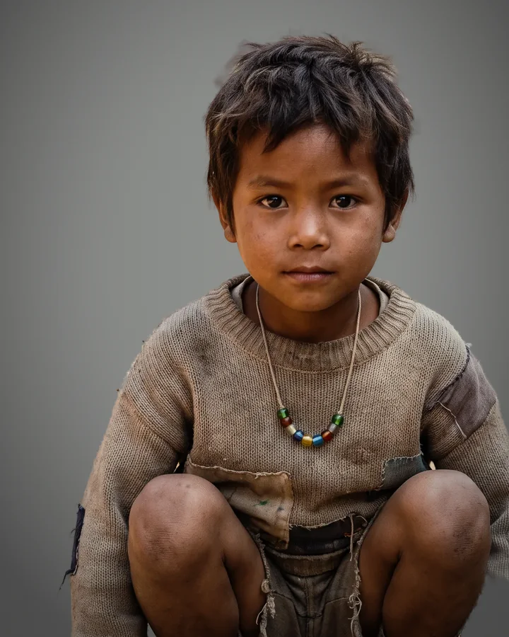 Pel, a small boy in a worn sweater crouched in a dirt lane